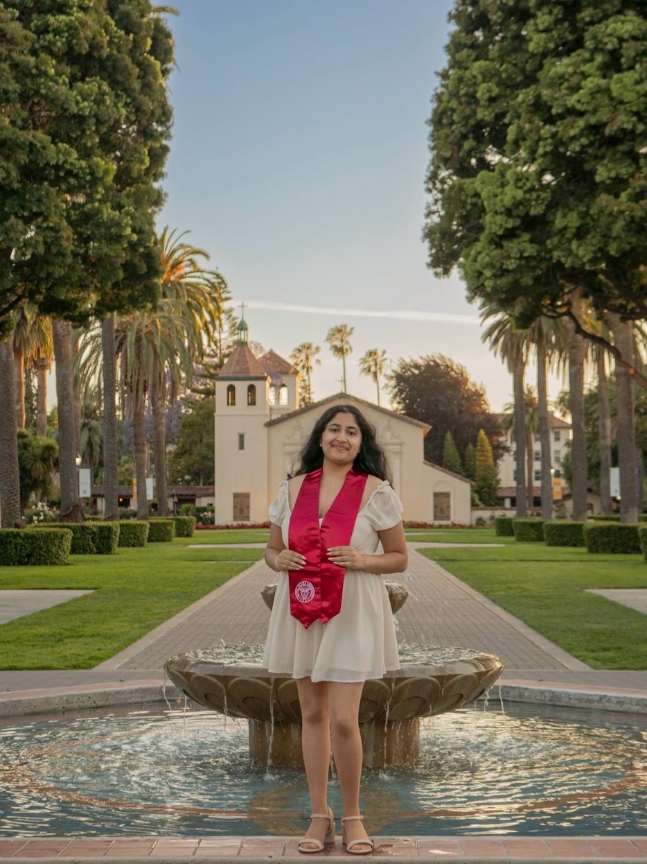 Divya Bengali standing on the Santa Clara University campus in graduation attire.